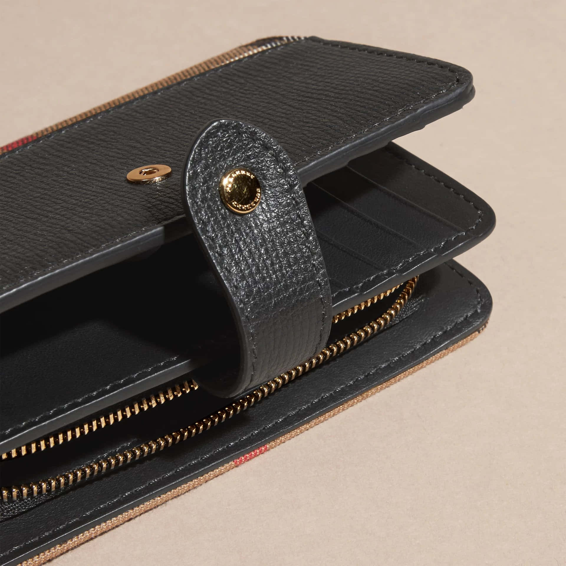 Black Leather 桌布 壁紙 — 黑色紋理皮革錢包特寫，配有金色拉鍊和黃銅五金件，背景為米色。