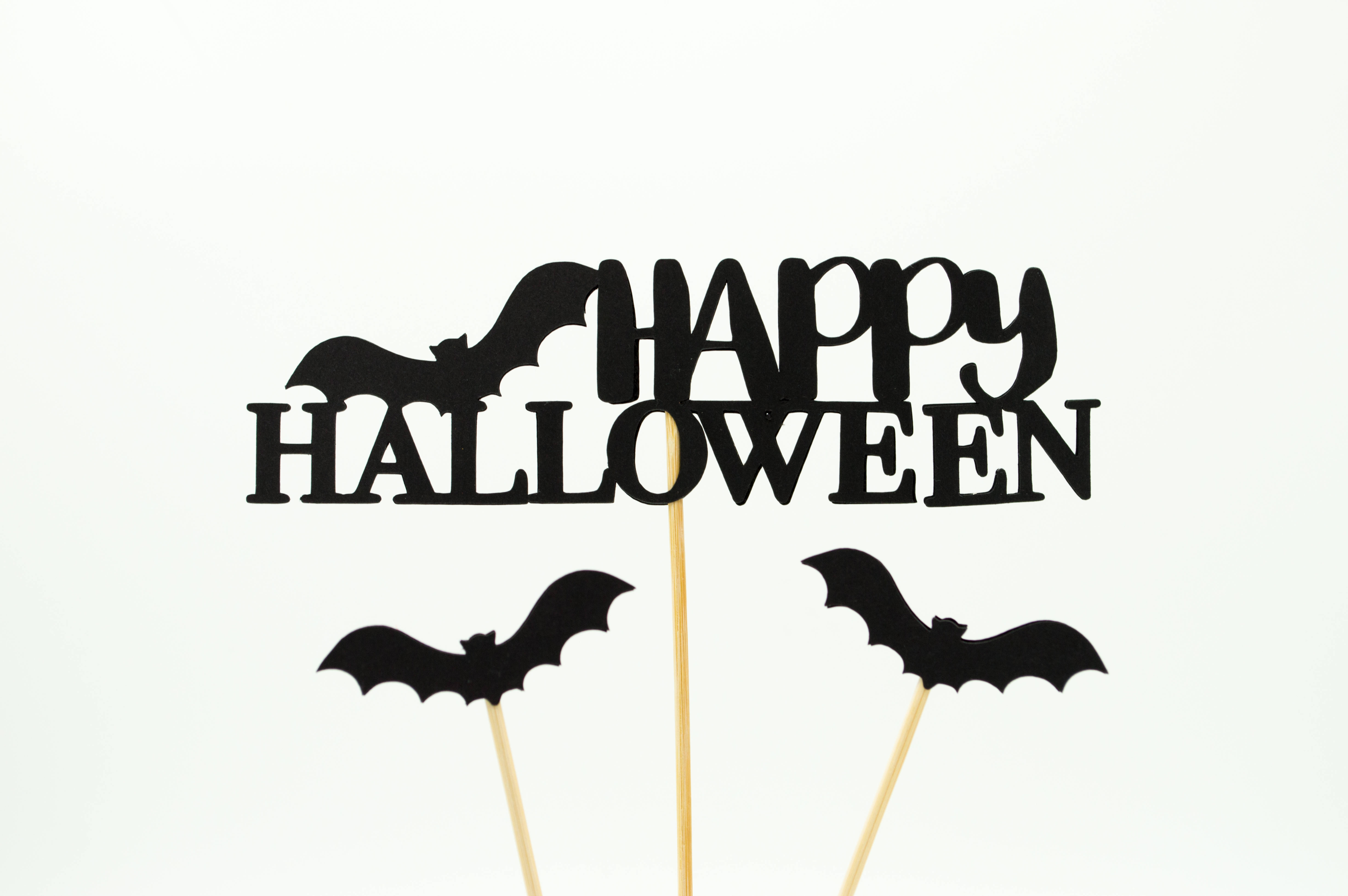 萬聖節動圖 桌布 壁紙 — 黑色紙剪萬聖節蛋糕裝飾，帶有「Happy Halloween」文字和蝙蝠剪影，附有棒子，白色背景。