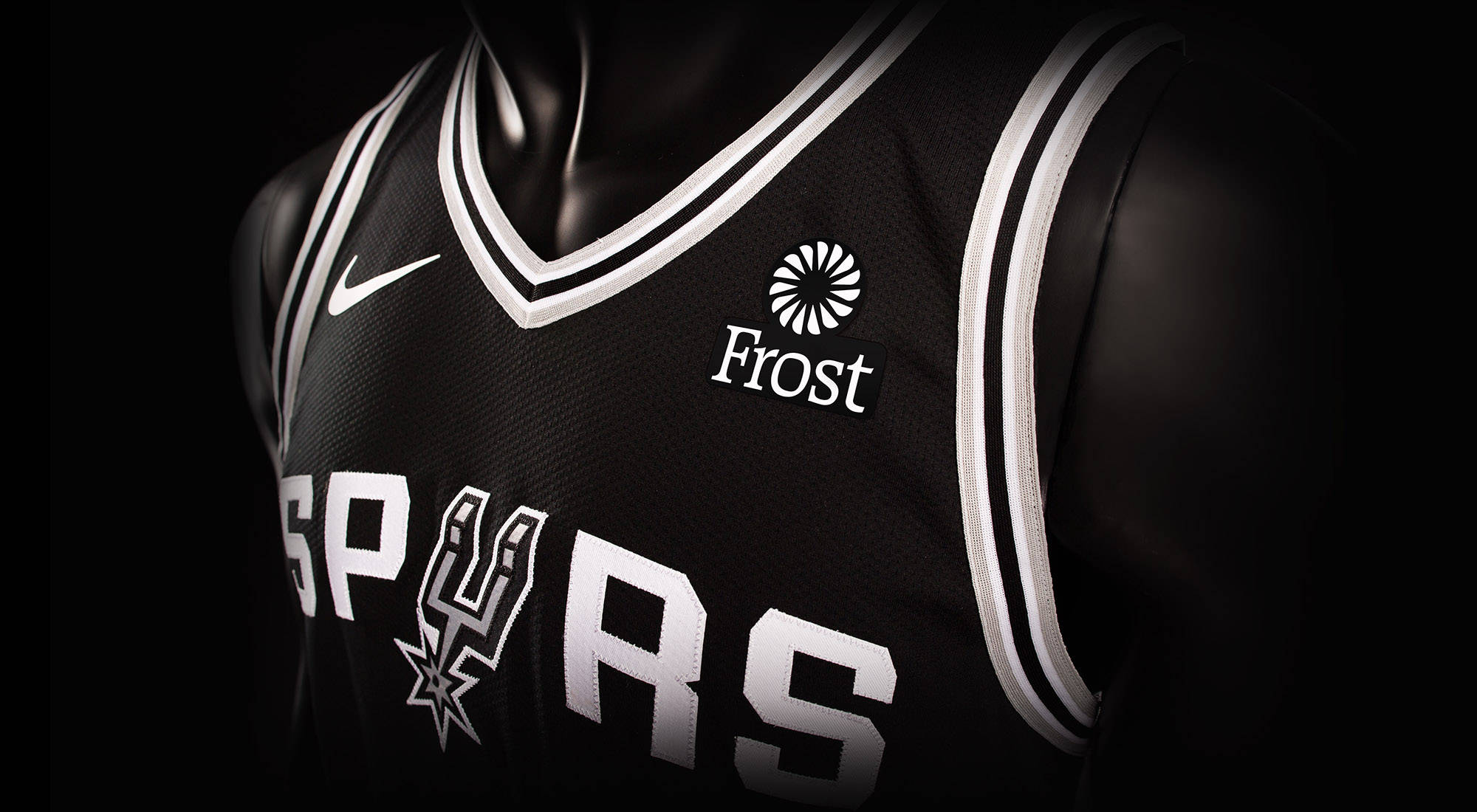 Spurs 桌布 壁紙 — 黑色聖安東尼奧馬刺籃球球衣特寫，帶有白色字體和Frost贊助商標誌，背景為深色。