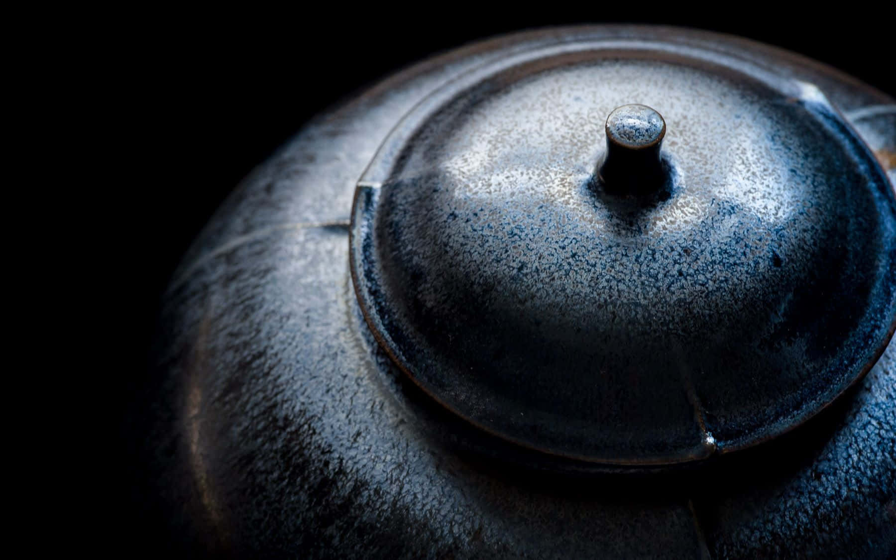 Ceramics 桌布 壁紙 — 黑色背景上，深藍色陶瓷茶壺蓋的特寫，帶有紋理釉面和金屬旋鈕。