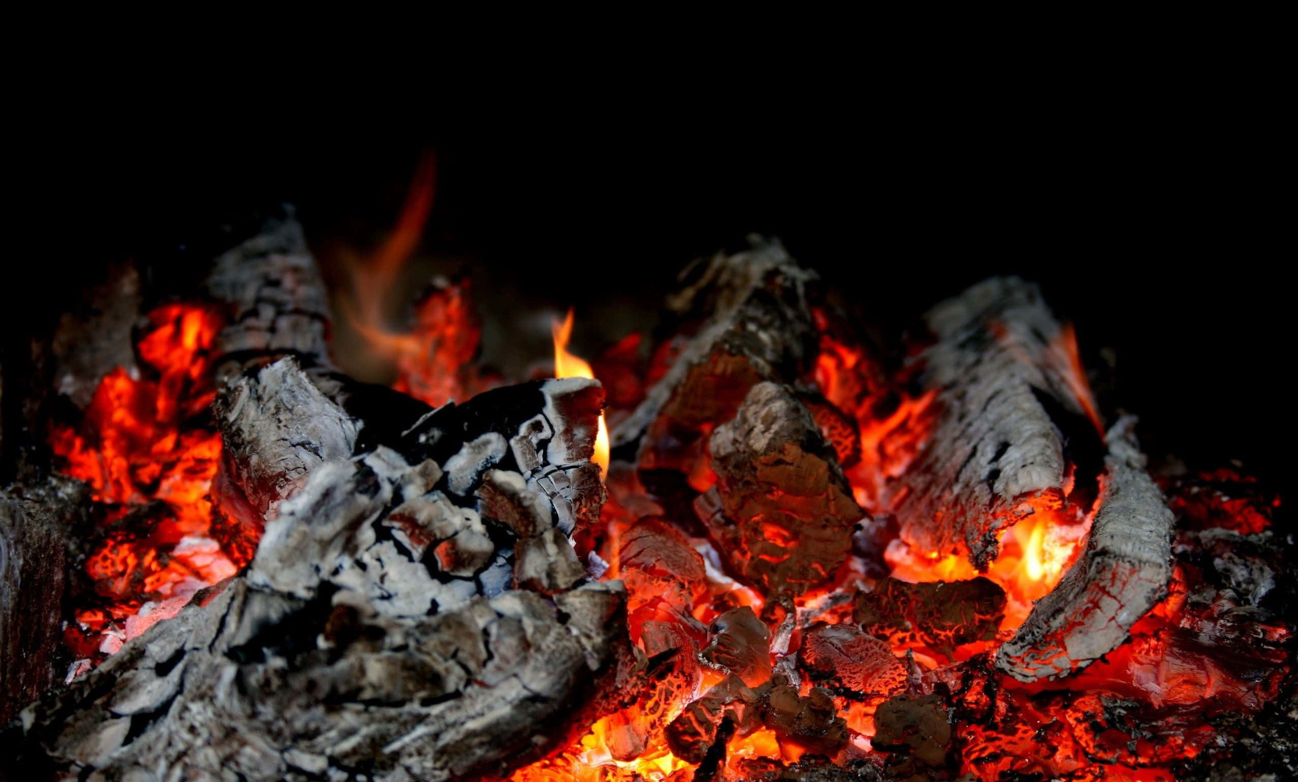 Charcoal 桌布 壁紙 — 黑色背景上，發光的餘燼和燒焦的木塊散發出強烈的紅色和橙色熱量的特寫。