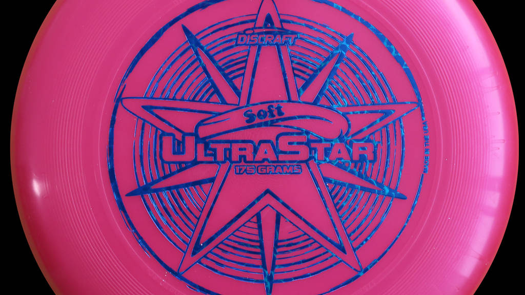 Ultimate Frisbee 桌布 壁紙 — 黑色背景上帶有藍色星星標誌的亮粉紅色Discraft UltraStar飛盤特寫。