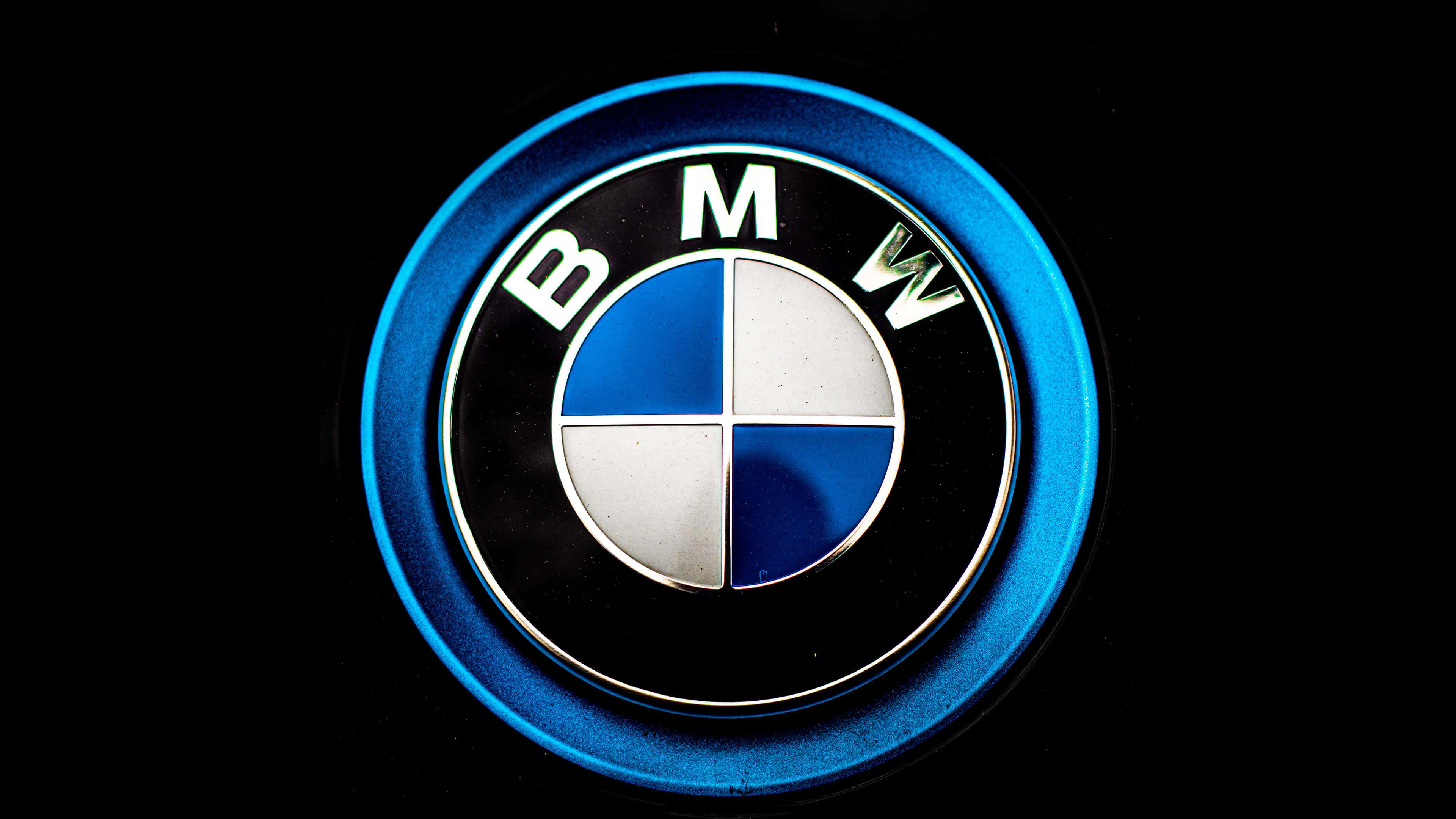 Bmw Logo 桌布 壁紙 — 黑色背景上帶有金屬光澤的發光藍色BMW標誌徽章的近距離特寫。
