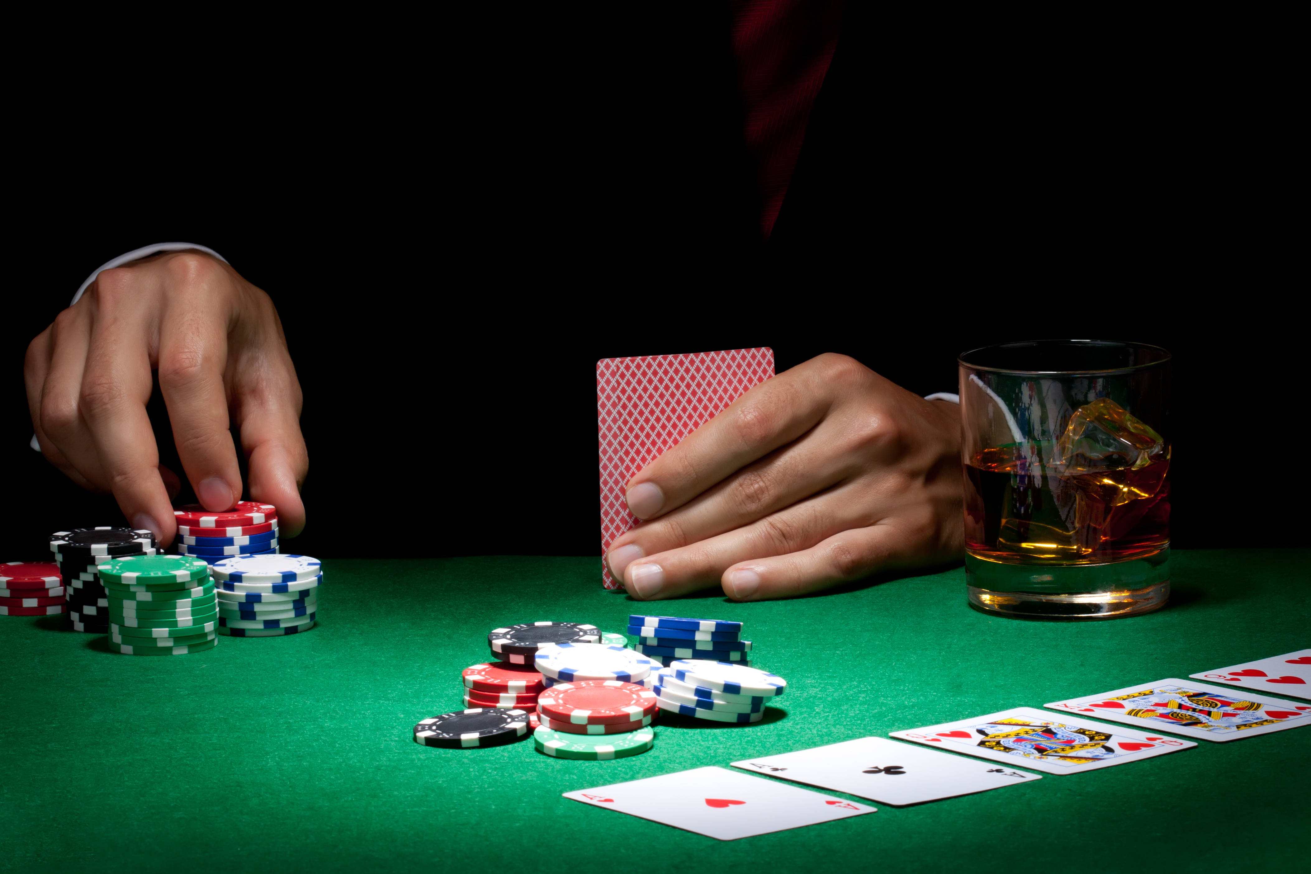 Poker 桌布 壁紙 — 黑色背景下的綠色氈桌上，手部特寫玩撲克牌，配有籌碼、紙牌和威士忌杯。