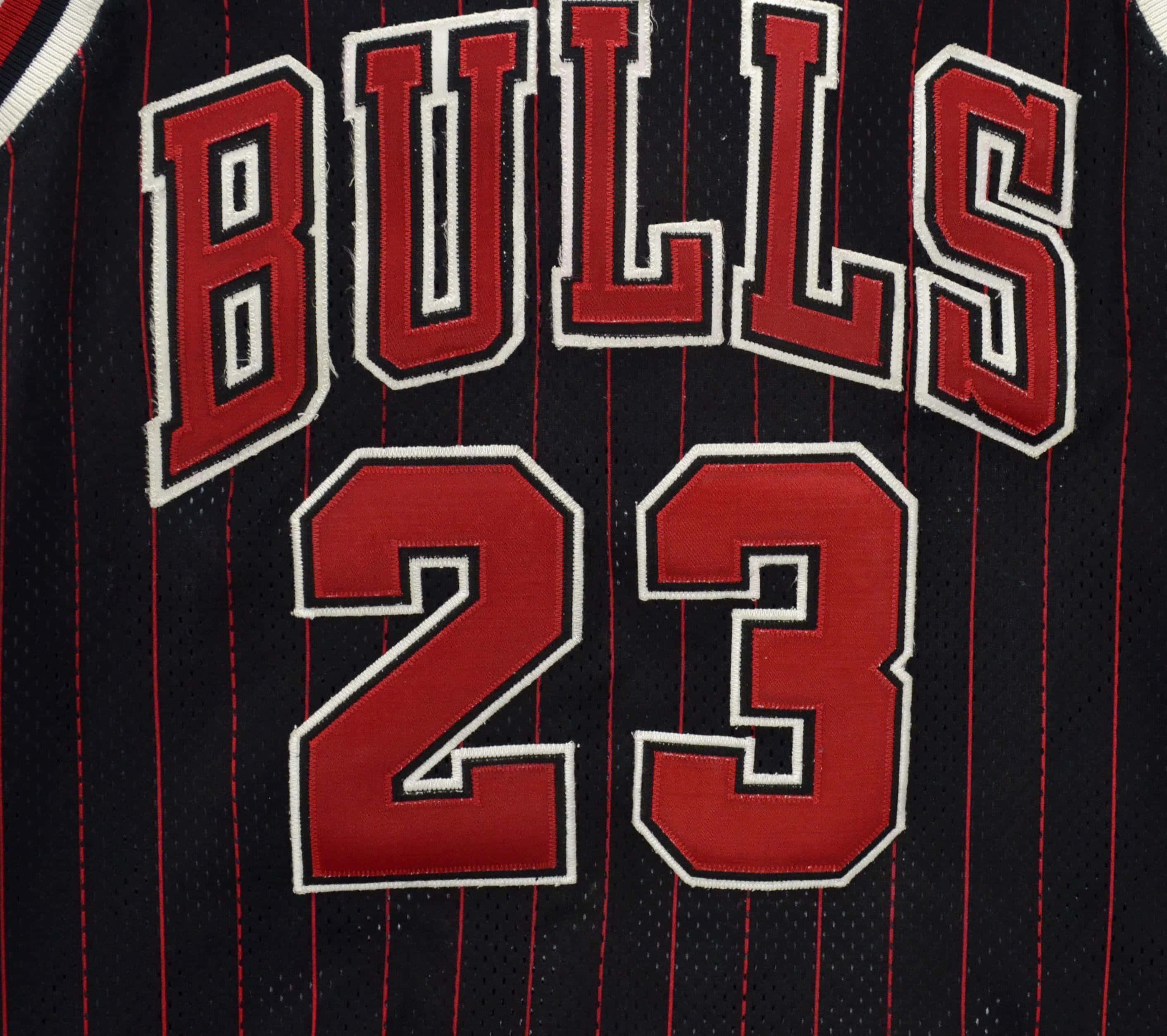 桌布 壁紙 — 黑色芝加哥公牛隊球衣特寫，帶有紅色和白色的「BULLS」以及粗體縫線的「23」號碼。