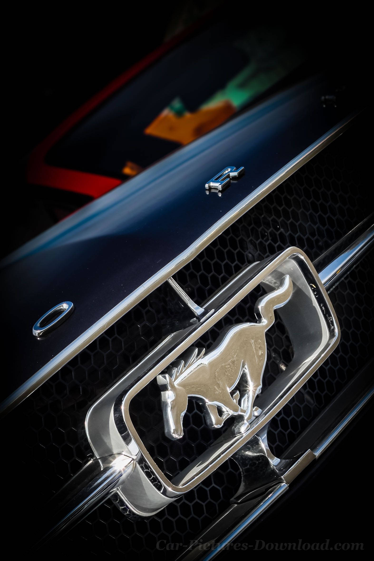 ford iPhone 桌布 壁紙 — 黑色蜂巢式格柵上閃亮鍍鉻野馬標誌的特寫，配以戲劇性燈光。