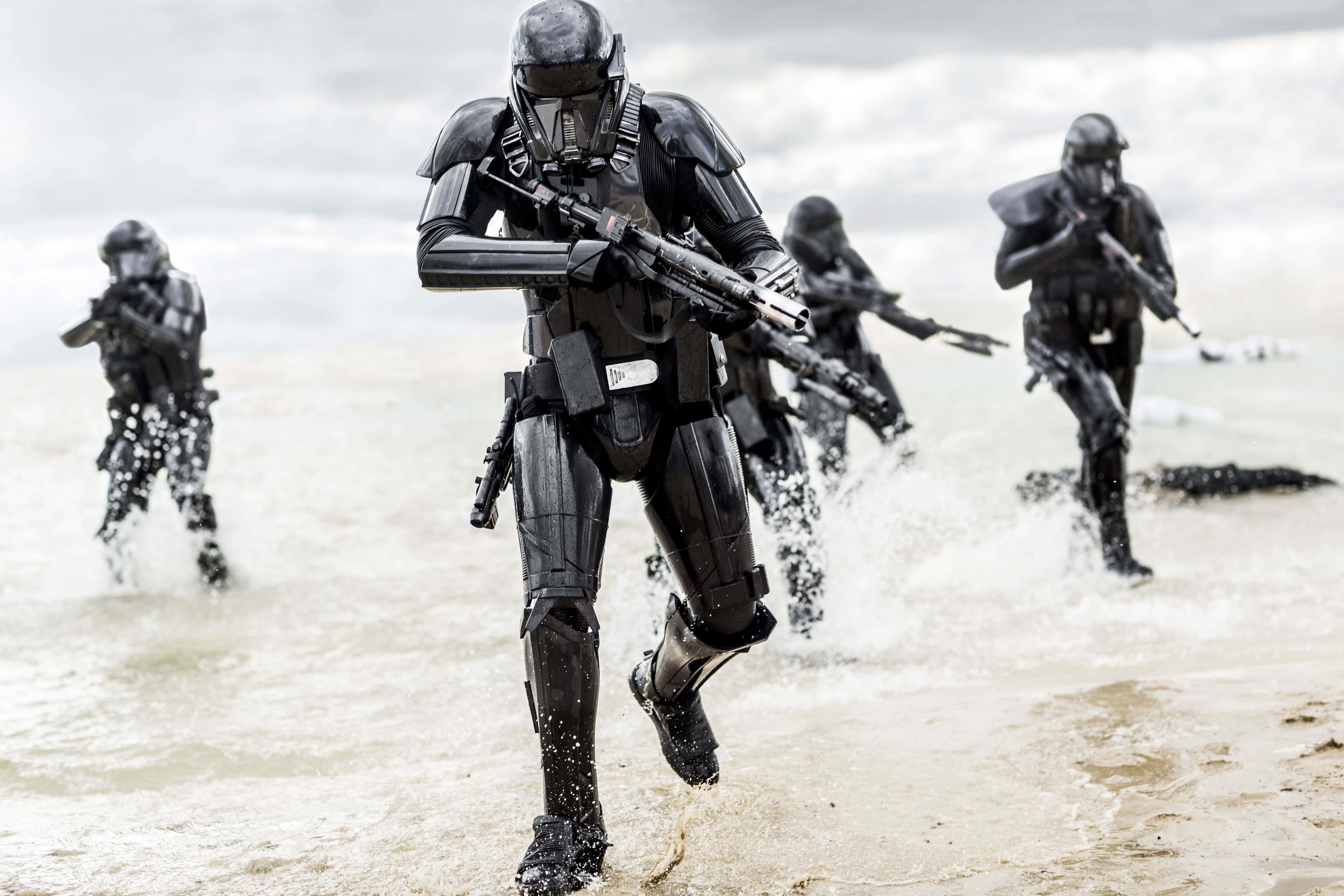 Blaster Rifles 桌布 壁紙 — 黑色裝甲士兵衝過暴風雨海灘的淺水區，波浪飛濺，天空陰沉。