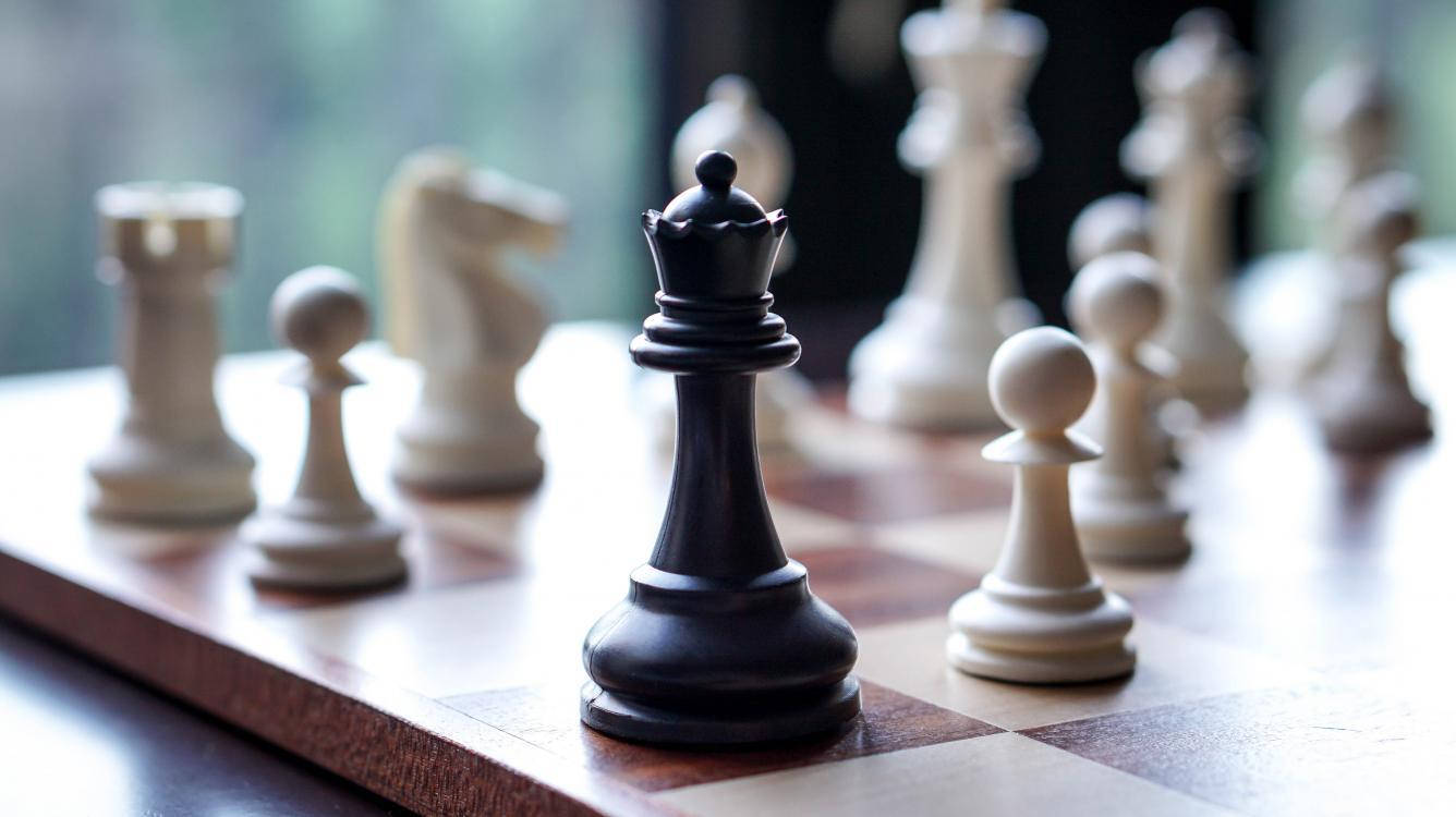 西洋棋 桌布 壁紙 — 黑色西洋棋國王特寫，高高矗立在木製棋盤上，背景有模糊的白色棋子。