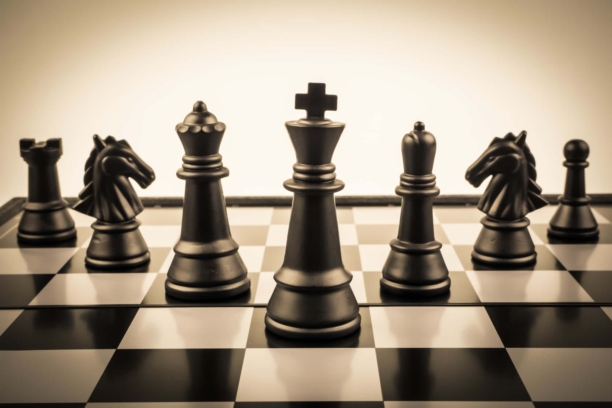 Chessboard 桌布 壁紙 — 黑色西洋棋棋子在一排棋盤上，在溫暖的工作室燈光下排列。