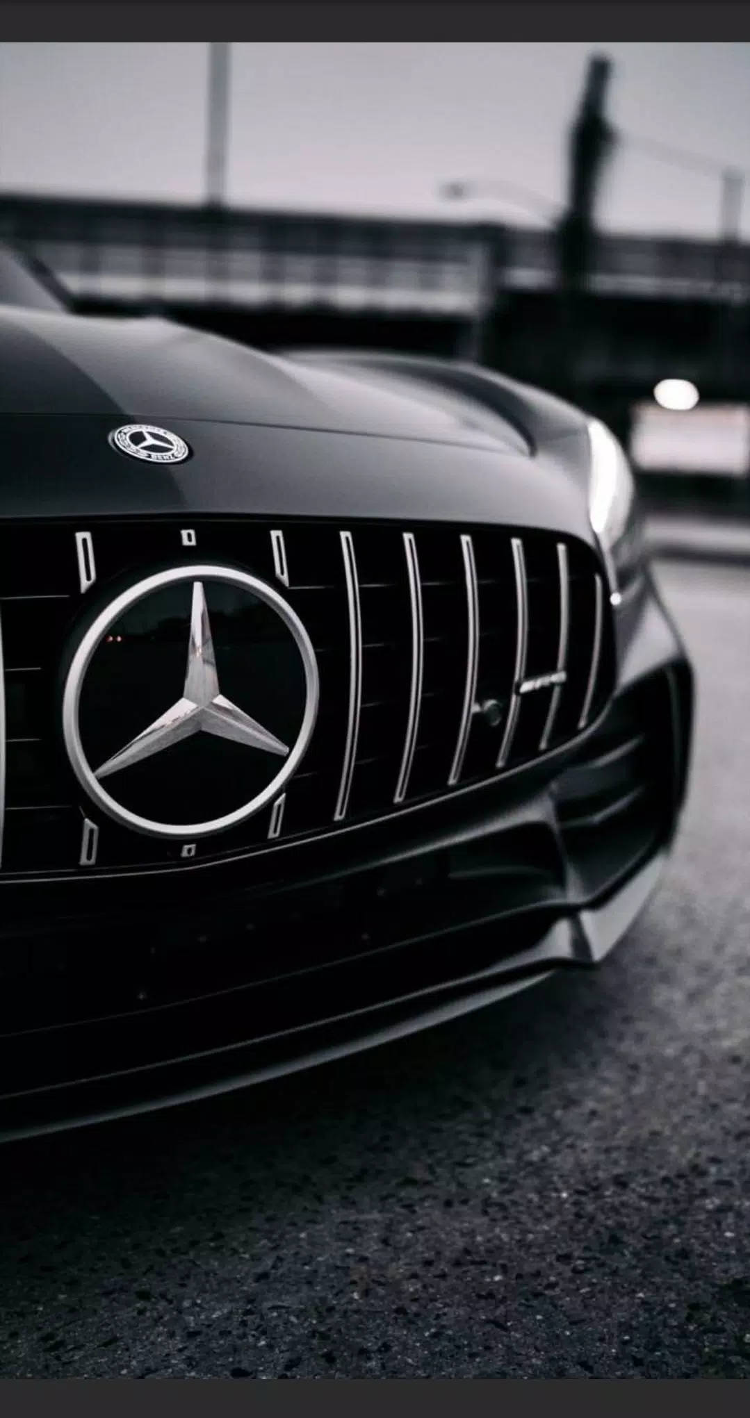 Mercedes 桌布 壁紙 — 黑色賓士AMG水箱護罩特寫，帶有鍍鉻飾邊，背景為模糊的城市景觀。