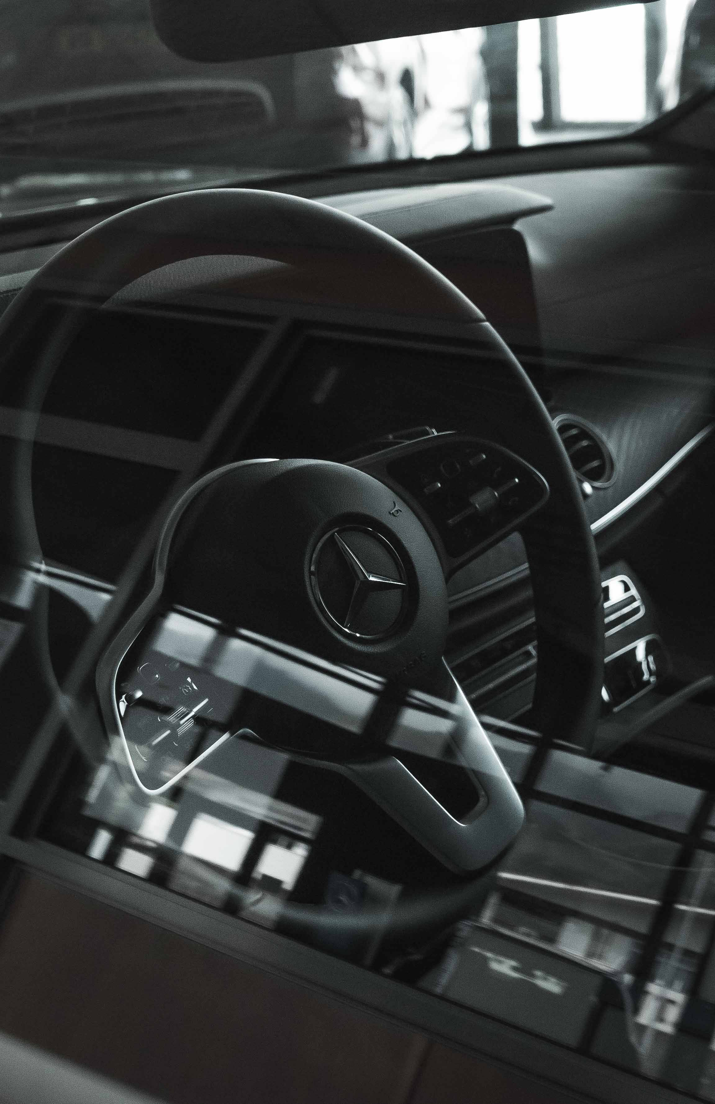 mercedes amg iPhone 桌布 壁紙 — 黑色賓士方向盤特寫，帶有鍍鉻裝飾和現代儀表板控制。