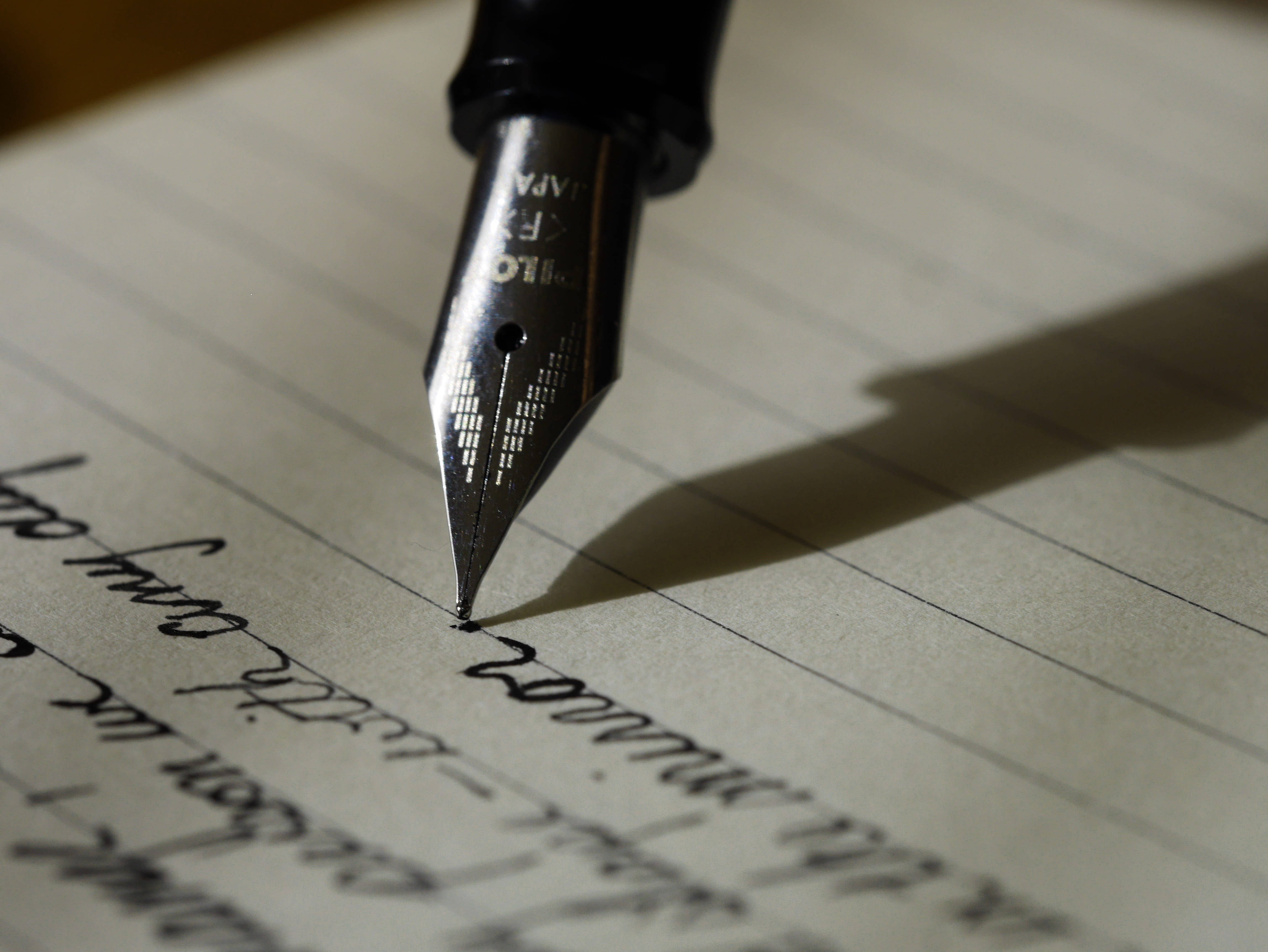 Cute Writing 桌布 壁紙 — 黑色鋼筆筆尖在暖光下於橫線紙上書寫優雅草寫的特寫。