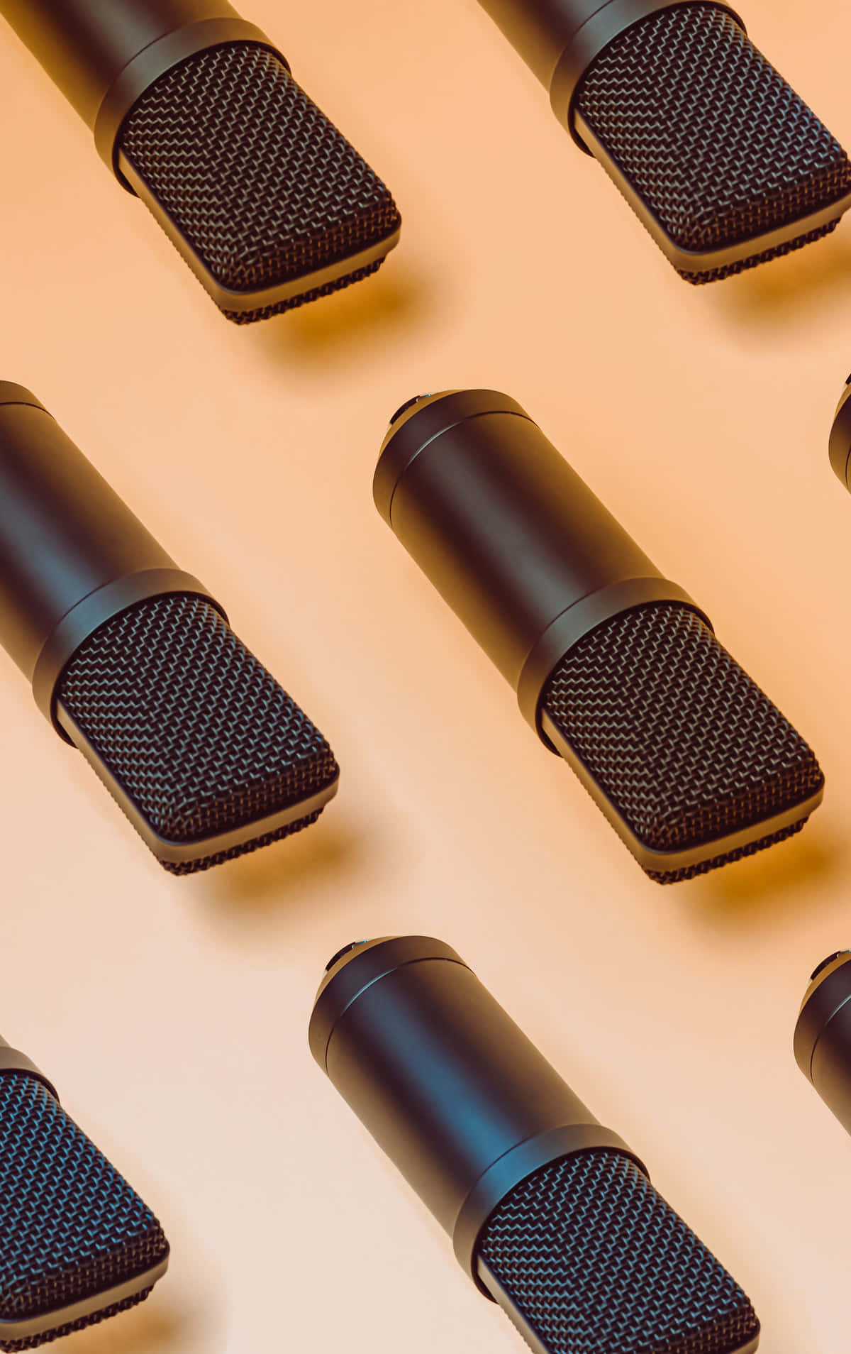 Microphones 桌布 壁紙 — 黑色錄音室麥克風在溫暖的蜜桃色背景上以對角線排列，帶有柔和陰影。