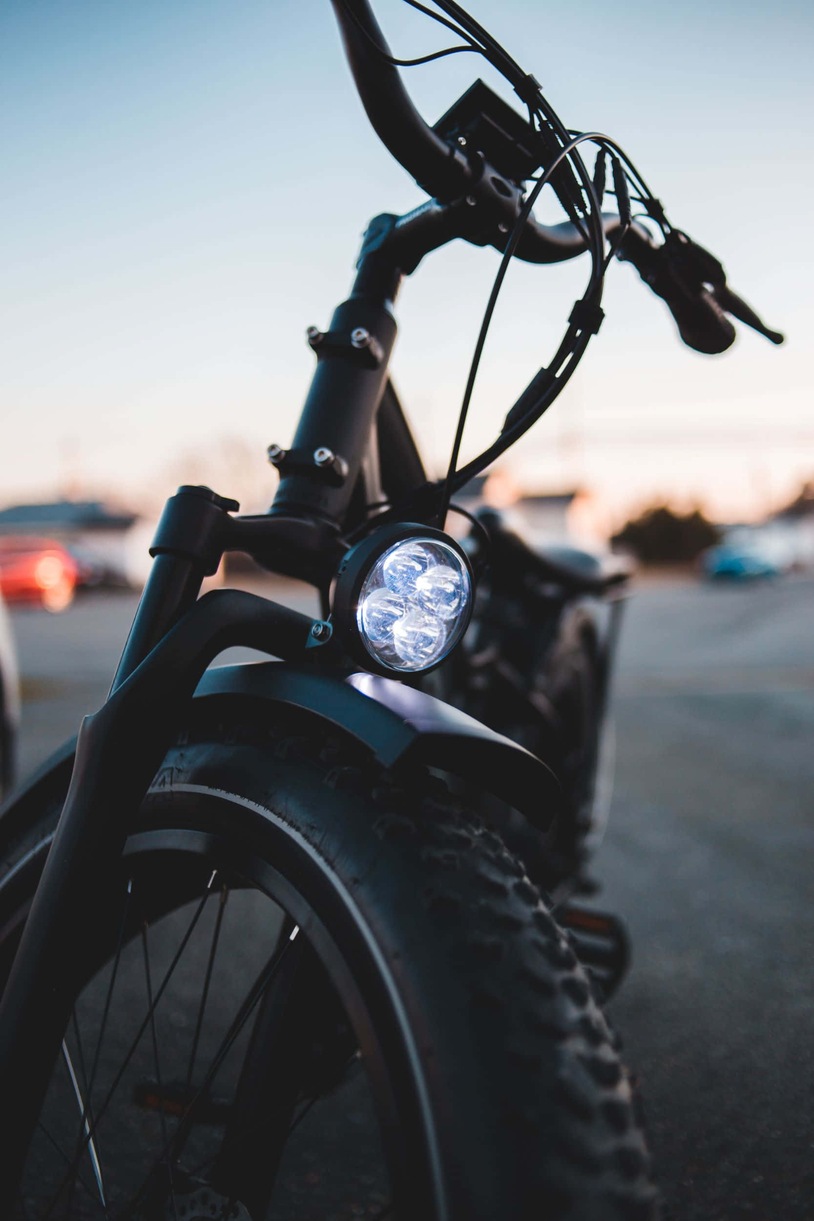 Electric Bike 桌布 壁紙 — 黑色電動自行車的手把和明亮頭燈在柔和日落天空下的特寫。