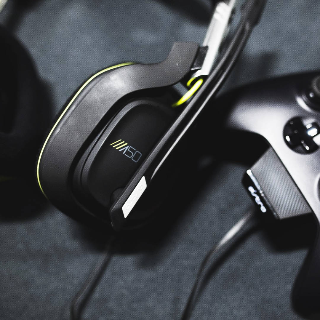 Xbox 桌布 壁紙 — 黑色電競耳機特寫，帶有螢光黃色點綴，放在深色布料上的控制器旁邊。