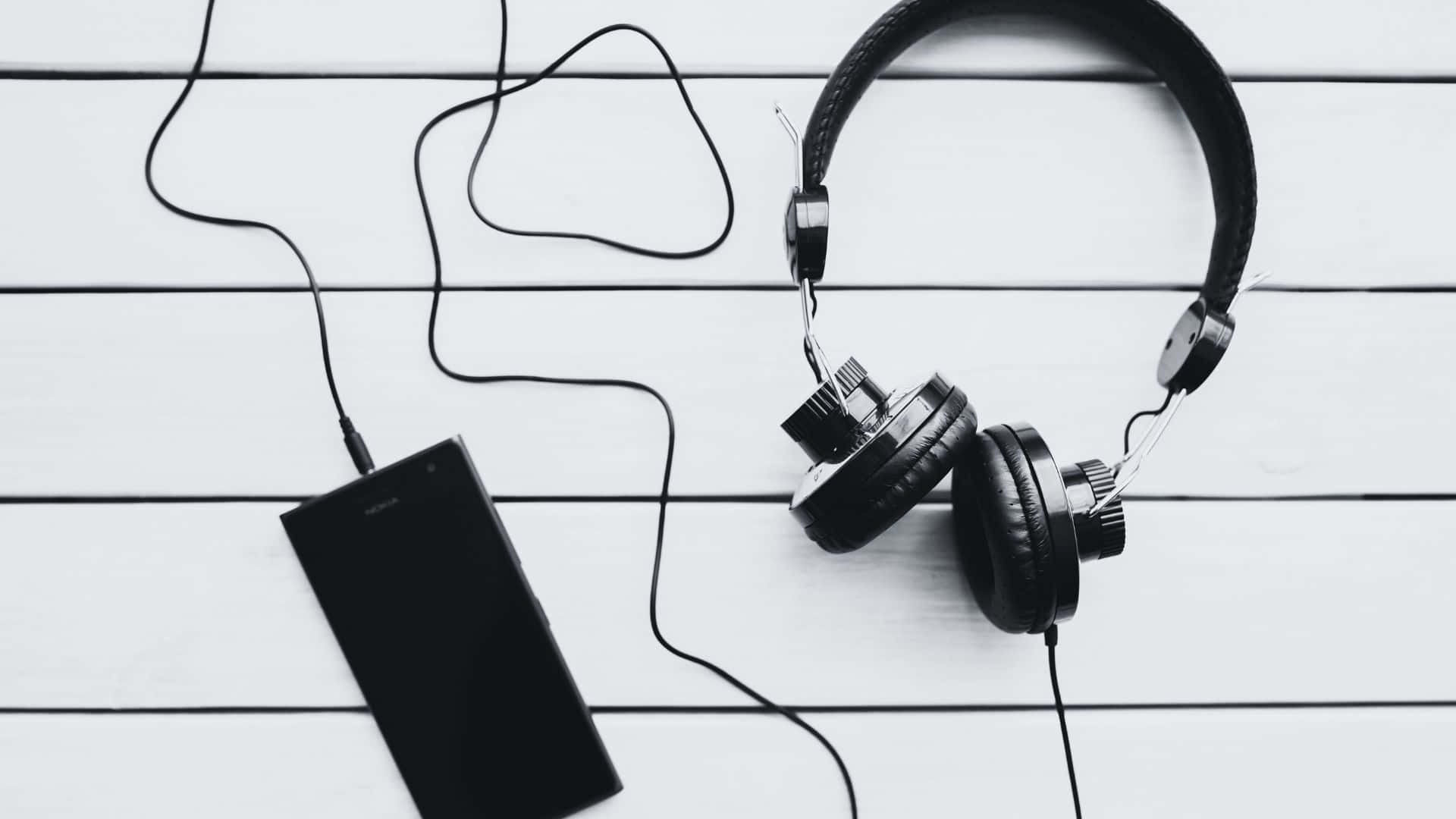 Black And White Music 桌布 壁紙 — 黑色頭戴式耳機和智慧型手機以單色調放在白色木板上。