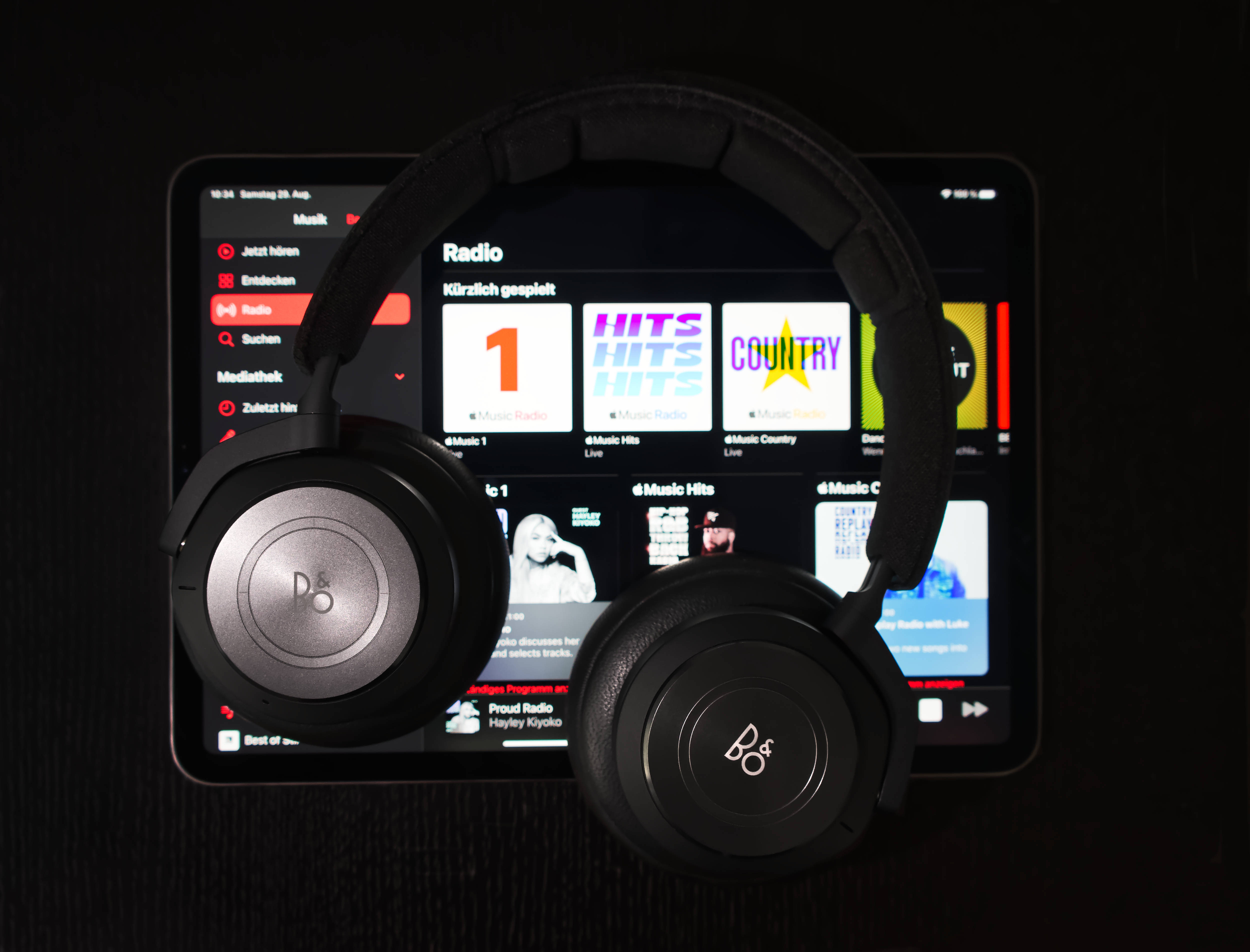 iOS 14 桌布 壁紙 — 黑色頭戴式耳機放在一部顯示音樂收音機應用程式的平板電腦上，應用程式有色彩繽紛的電台方塊，背景為深色木質表面。