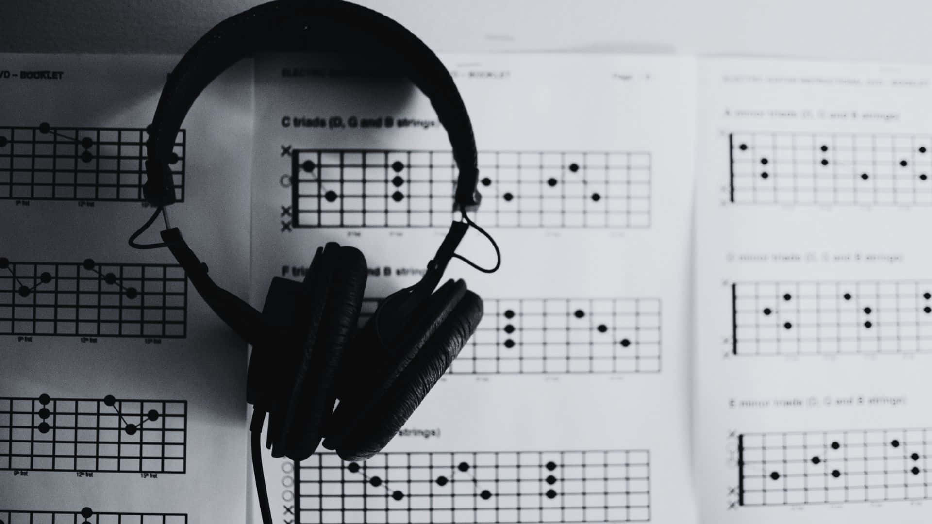 Black And White Music 桌布 壁紙 — 黑色頭戴式耳機放在單色構圖的吉他和弦圖譜上。