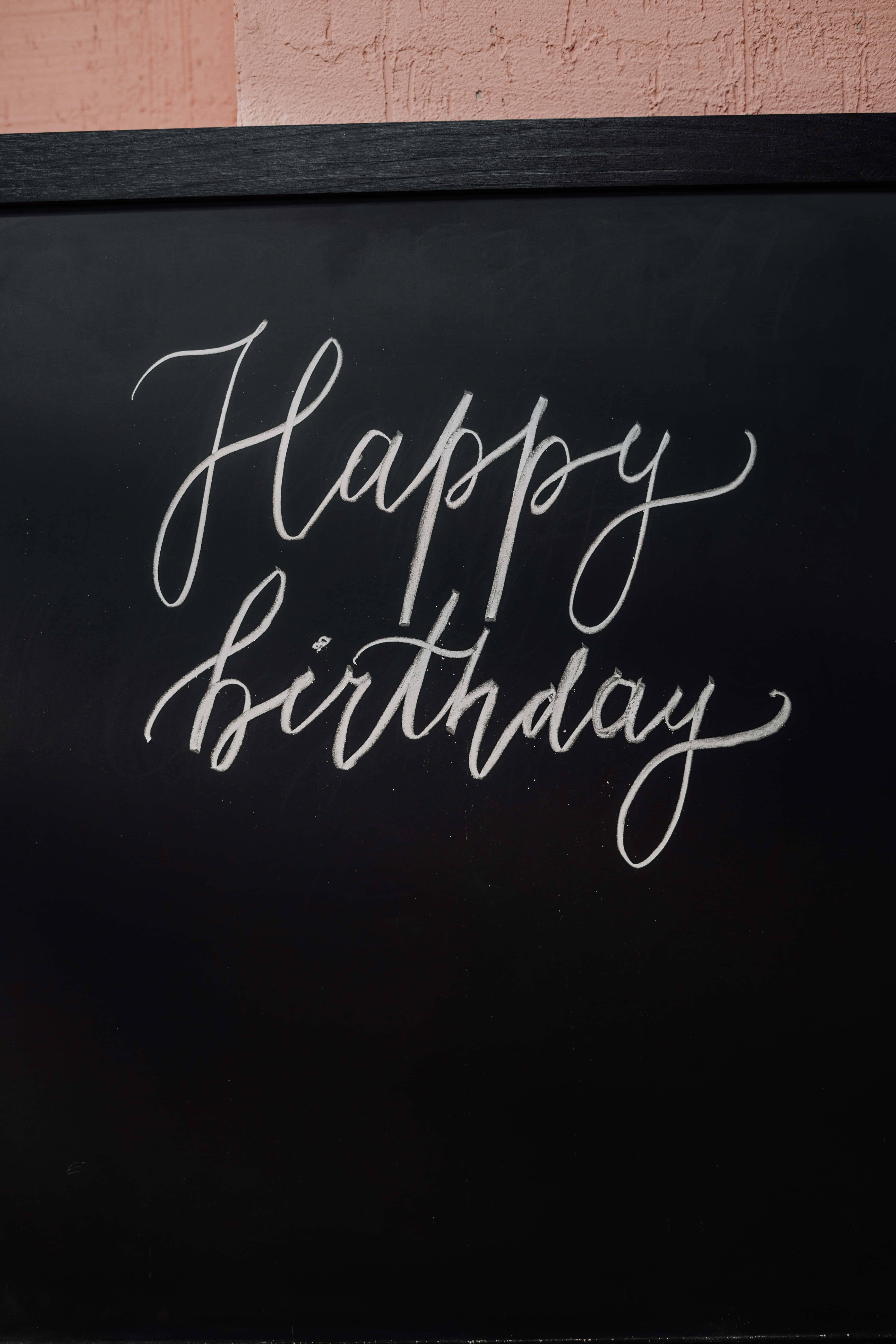 High Resolution Happy Birthday 桌布 壁紙 — 黑色黑板上優雅的白色草書 'Happy Birthday'，上方有紋理的粉紅色牆壁。