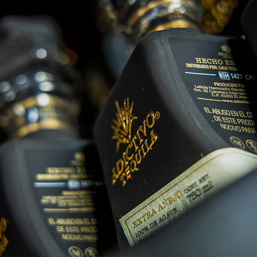 高清 桌布 壁紙 — 黑色龍舌蘭酒瓶特寫，帶有金色字體和標籤，顯示「Extra Añejo」和「100% de Agave」，背景為深色模糊。
