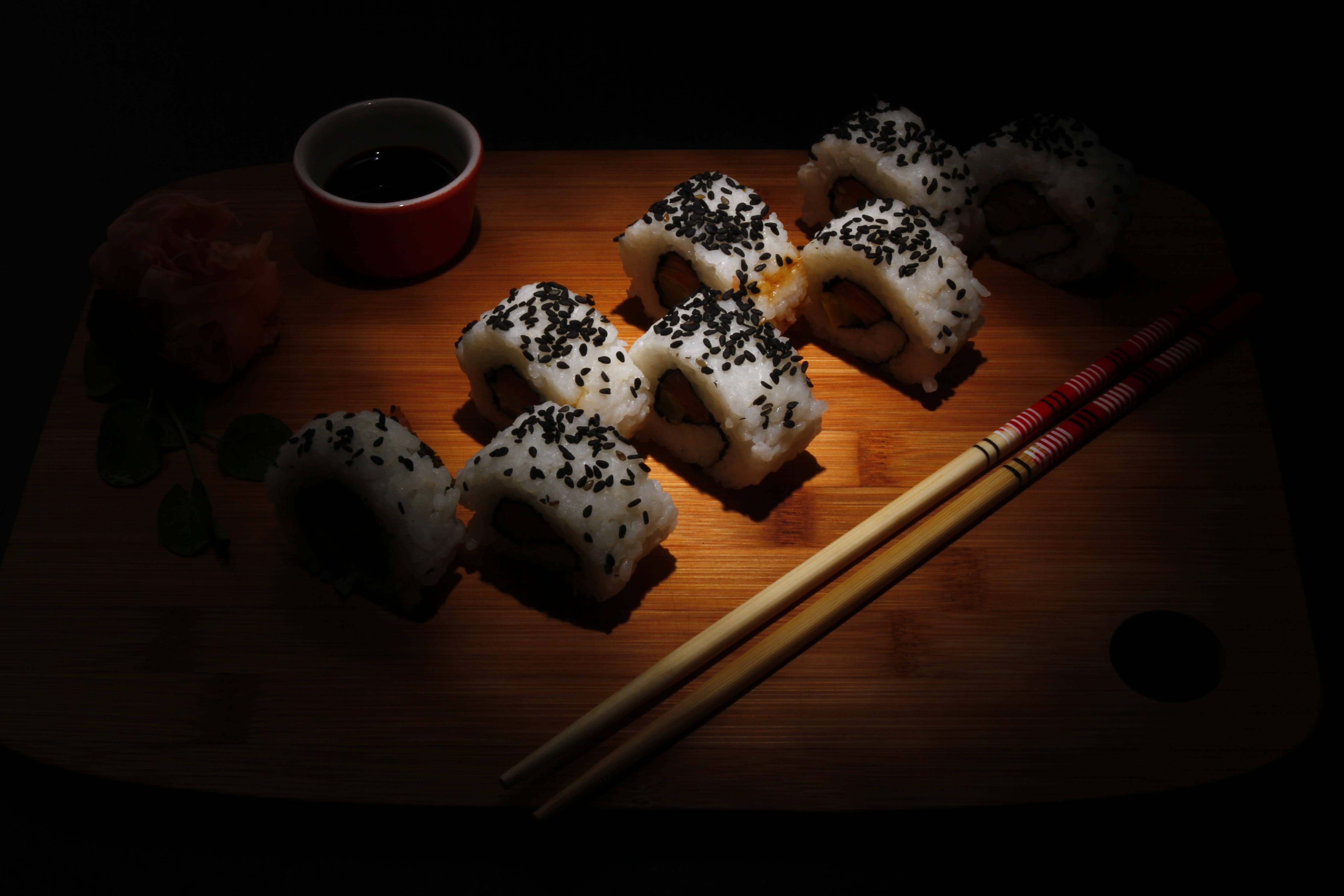 Sushi 桌布 壁紙 — 黑芝麻壽司捲在戲劇性的聚光燈下，在木板上與筷子及醬油一起發光。