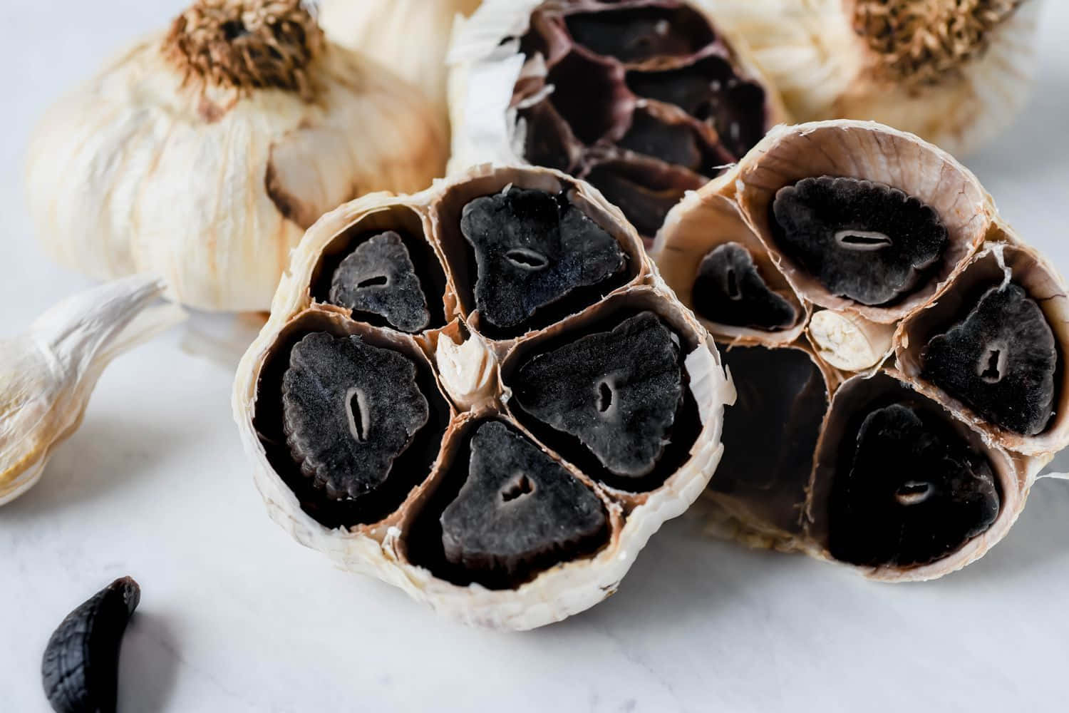 Black Garlic 桌布 壁紙 — 黑蒜瓣切開的特寫，在白色大理石背景上露出深色光澤的內部。