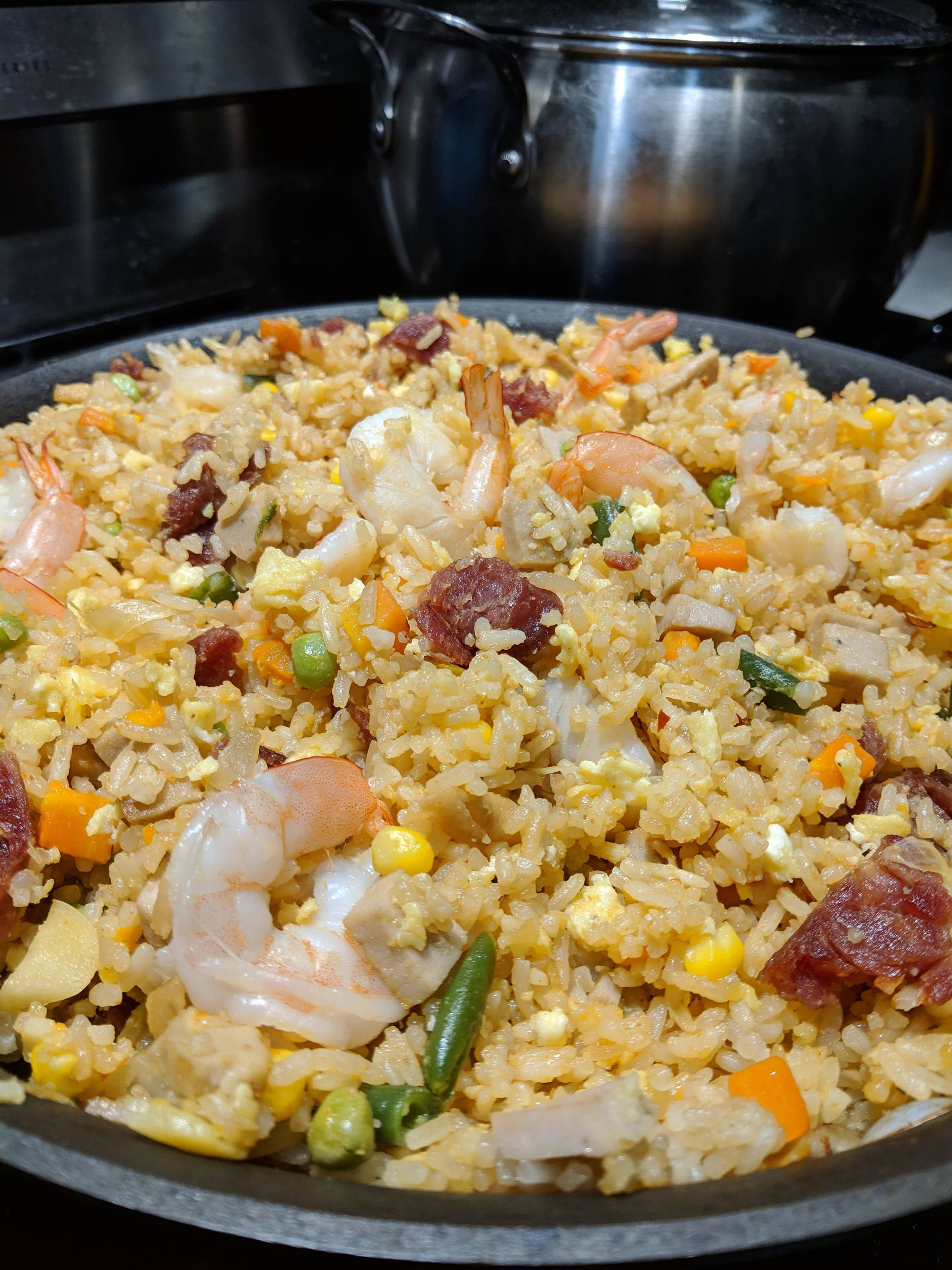 烹飪 桌布 壁紙 — 黑鍋中金黃色炒飯配蝦仁、玉米、青豆和香腸的特寫，置於爐灶上。