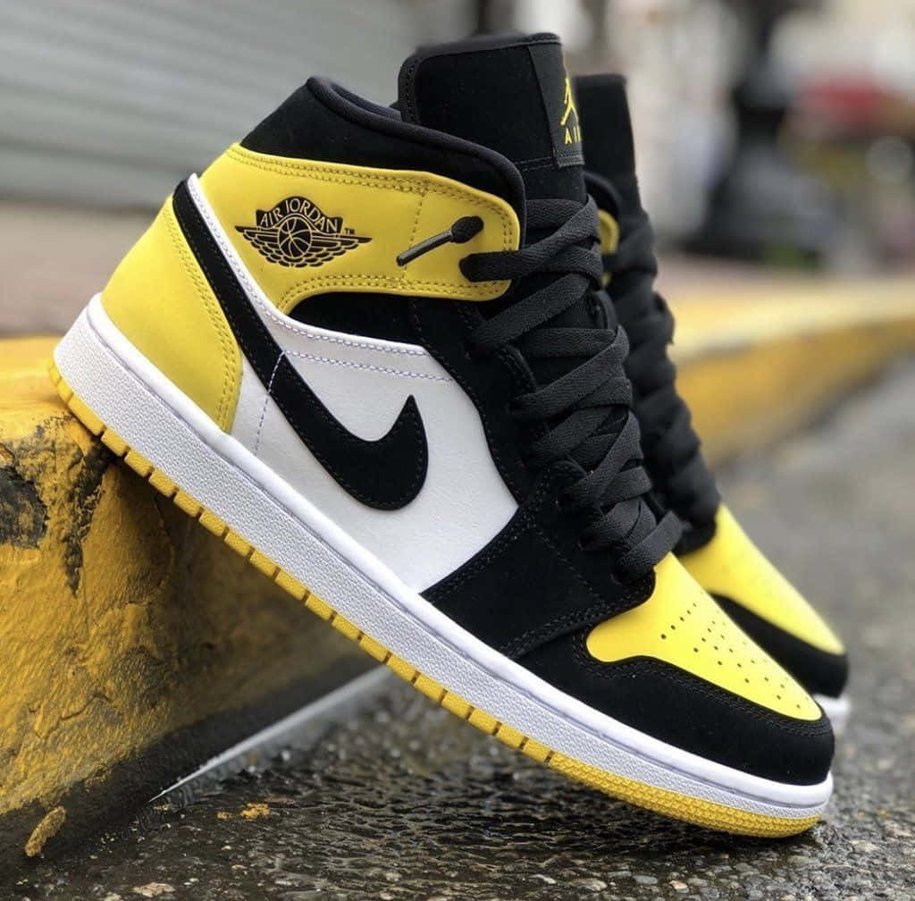 鞋子 桌布 壁紙 — 黑黃色 Air Jordan 1 運動鞋放在一條風化的黃色路緣石上，背景是模糊的城市景觀。