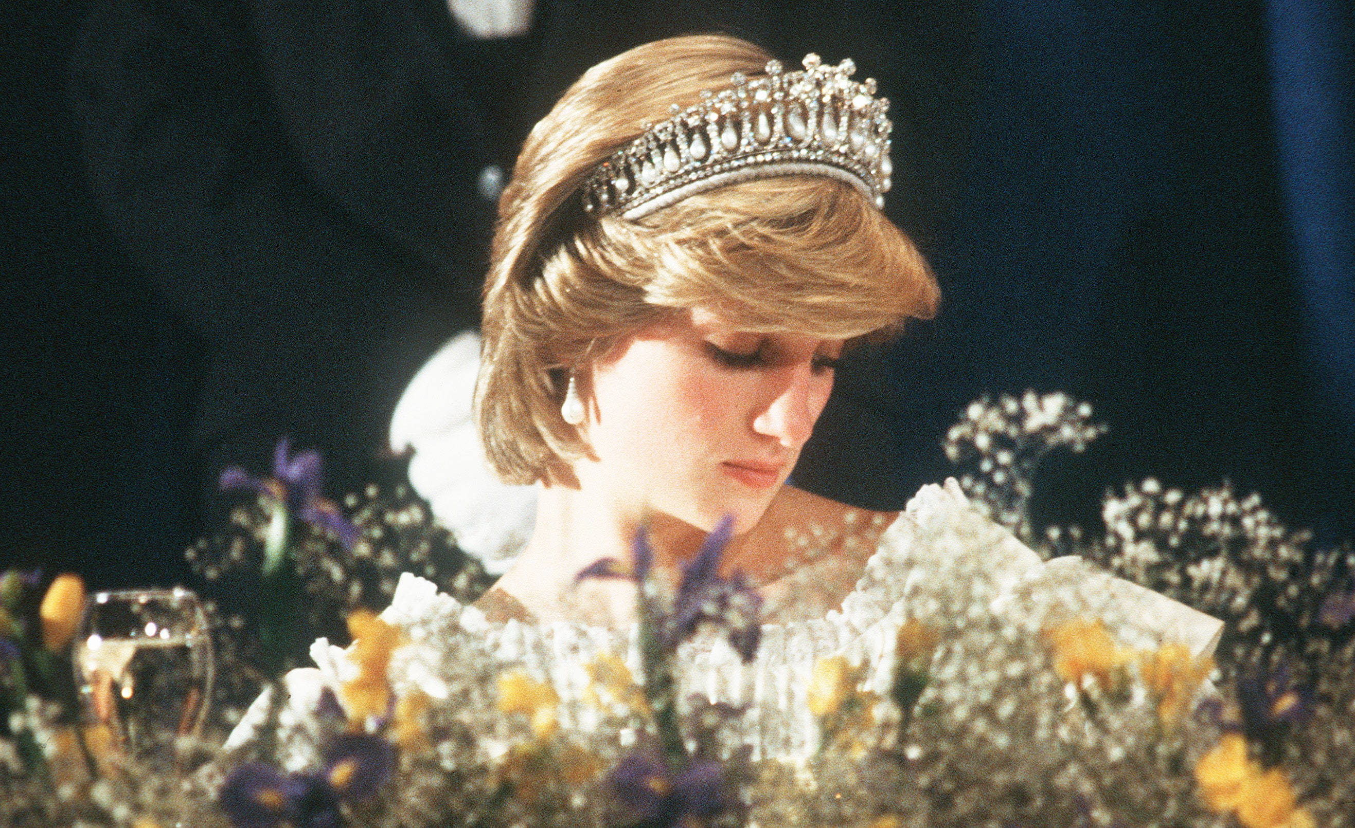 Princess 桌布 壁紙 — 黛安娜王妃低頭凝視，戴著閃閃發光的頭飾，周圍環繞著鮮豔的紫色、黃色和白色花朵。