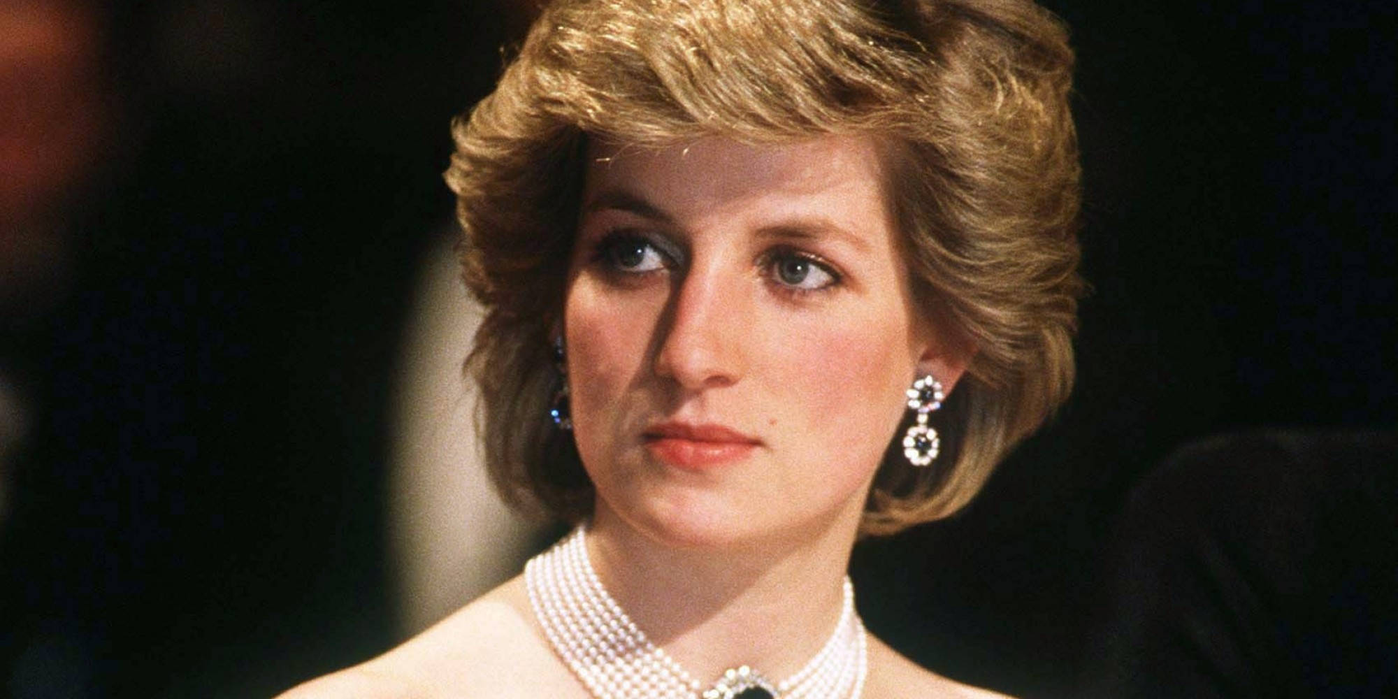Princess 桌布 壁紙 — 黛安娜王妃在特寫肖像中若有所思地凝視，佩戴珍珠項鍊和鑽石耳環，背景為深色。