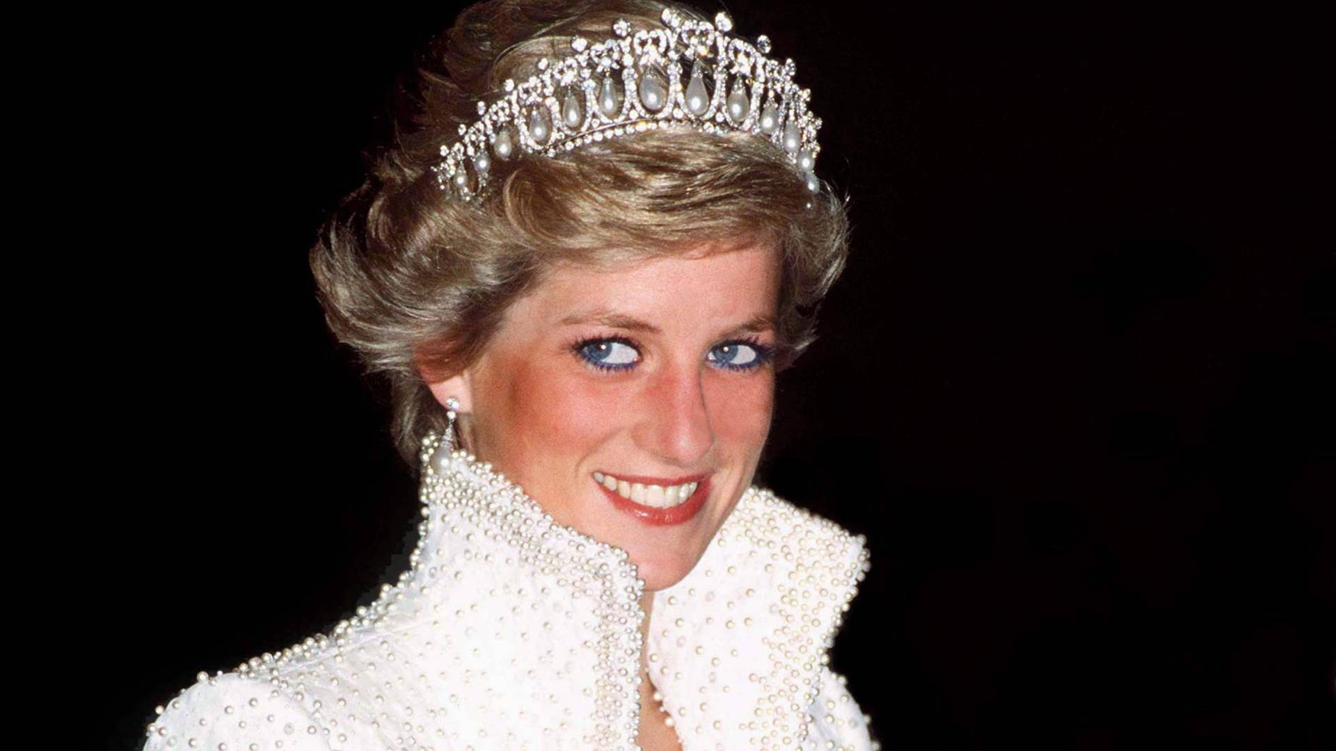 Princess 桌布 壁紙 — 黛安娜王妃戴著鑲有珍珠的頭飾和相配的珍珠點綴白色服裝，在黑色背景前溫暖地微笑。