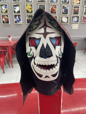 一個色彩繽紛的 lucha libre 面具，帶有骷髏設計，放在餐廳的紅色底座上。 — Kindle 壁紙