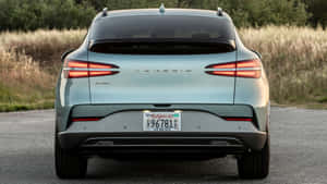 淺藍色 Genesis GV60 電動 SUV 在乾草和樹木道路上的後視圖。 — 創世紀 壁紙