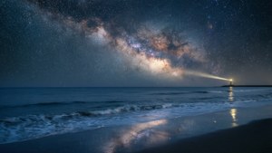 燈塔光束劃破銀河下海洋上空的星空