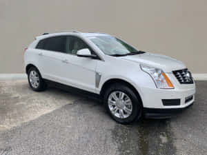 白色Cadillac SRX SUV停放在米色牆壁附近的濕路面上。 — 凱迪拉克 壁紙