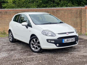 白色Fiat Punto停在碎石上，靠近磚牆和綠色植物。 — 飛雅特 壁紙