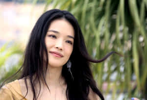 一位長著深色長髮的女性，在戶外身後有綠植的環境中輕柔微笑。 — 尚氣 壁紙