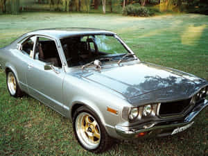 銀色經典跑車配金色輪圈，停放在綠色草地上。 — 馬自達 壁紙