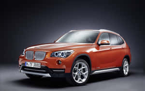 橙色BMW X1 SUV在工作室燈光下，深色背景。 — MacBook Pro 13 壁紙
