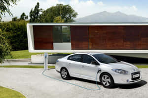 銀色電動車連接到充電器，靠近現代房屋，後面有山。 — 雷諾 壁紙