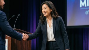 一位身穿套裝的女士在簡報期間與一位男士在講台上握手。