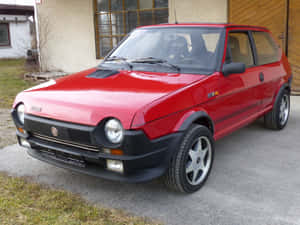 紅色菲亞特126p停在混凝土車道上，靠近木製車庫。 — 飛雅特 壁紙