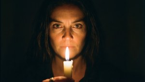 一個女人在黑暗的房間裡拿著一支點燃的蠟燭，她的臉被火焰照亮。