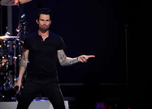 Adam Levine 在舞台上表演，指著並露出刺青。 — 省電 壁紙