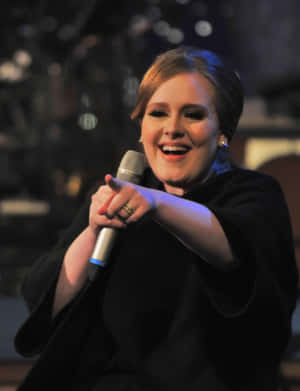 Adele 在舞台上燦爛微笑拿著麥克風。 — 瑪丹娜 壁紙