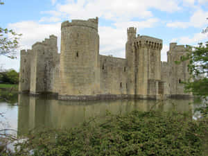 陽光明媚的日子裡，中世紀的石頭城堡被水和綠樹環繞。 — 博人 壁紙