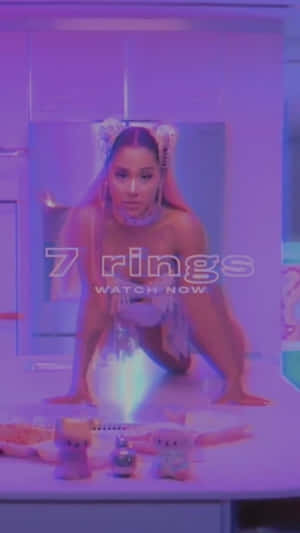 Ariana Grande 在一個紫色燈光的未來風格房間中，與毛絨玩具和發光戒指一起。 — 音樂錄影帶 壁紙