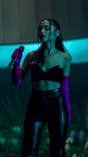 歌手 Ariana Grande 在藍色燈光下穿著黑色服裝和紫色手套在舞台上表演。 — 山坡 壁紙