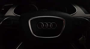 特寫 Audi 標誌在方向盤上，車廂昏暗，配有數位時鐘。 — 奧迪 GIF 壁紙