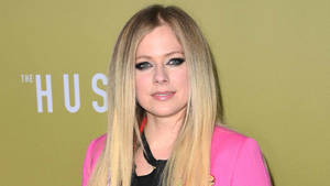 Avril Lavigne 在活動中穿著粉紅色西裝外套，背景為綠色。 — 艾薇兒·拉維尼 壁紙